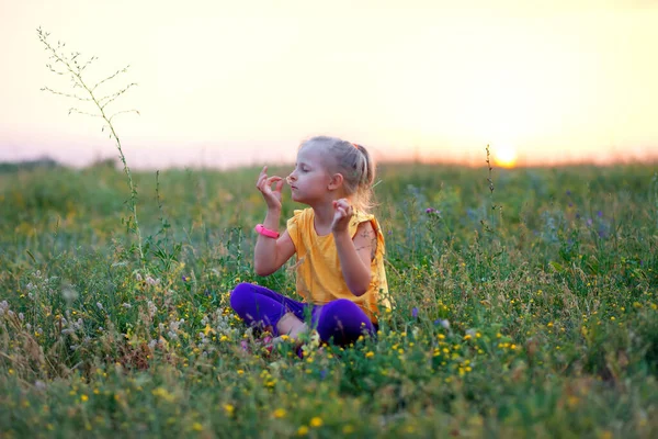 Yazın gün batımında bir çocuk bir tarlada oturur. Yazın açık hava eğlencesi. Temiz havada meditasyon. Çocuk yogası ve meditasyon. Psikolojik sağlık