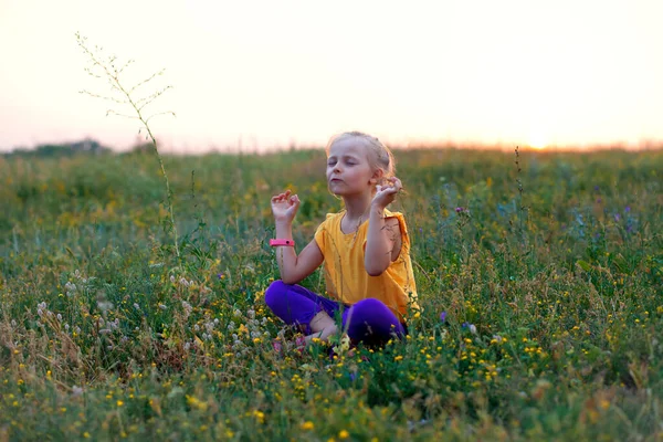 Yazın gün batımında bir çocuk bir tarlada oturur. Yazın açık hava eğlencesi. Temiz havada meditasyon. Çocuk yogası ve meditasyon. Psikolojik sağlık
