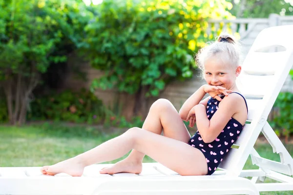 6-7 yaşlarında güzel bir kız gün batımında bahçede iskemlede dinleniyor. Bahçede dinlenme ve meditasyon, tatilde. Mutlu bir çocukluk, yaz tatilleri, çocuklarla kendi bahçelerinde karantina altında geçirilen yaz tatilleri.