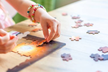 Bir kız masada oturur ve evde bir yapboz toplar. Eller yukarı. Oyun sayesinde öğreniyorum. Çocukların konsantrasyonunu öğreniyorum. Kötü hava koşullarında ve karantinada ailelerle evde oynarız.