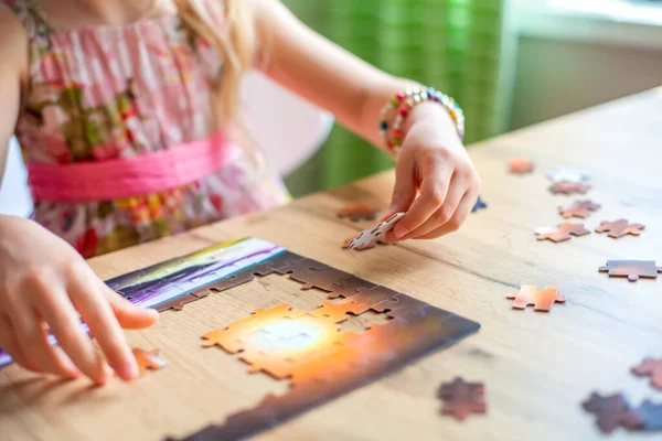 Bir kız masada oturur ve evde bir yapboz toplar. Eller yukarı. Oyun sayesinde öğreniyorum. Çocukların konsantrasyonunu öğreniyorum. Kötü hava koşullarında ve karantinada ailelerle evde oynarız.