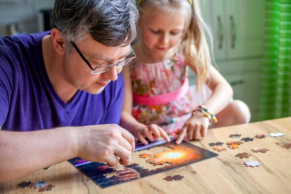 Bir kız masada oturur ve evde bir yapboz toplar. Kameraya bakar ve güler.