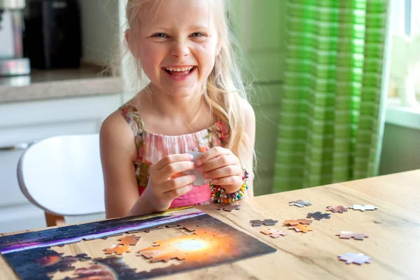 Bir kız masada oturur ve evde bir yapboz toplar. Kameraya bakar ve güler.