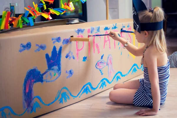 Korsan kostümlü bir kız kartondan yapılmış büyük bir ev yapımı deniz gemisi çiziyor. Tüm ailenin korsanlık oyunu, yaratıcı gelişim, macera ve seyahat hayalleri.