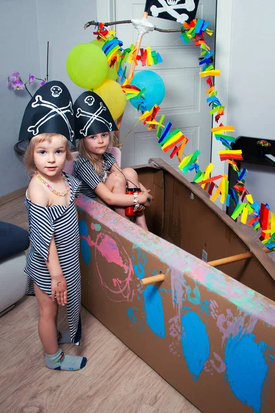 İki komik çocuk evdeki karton bir deniz gemisinde korsan kostümü giyip oynuyorlar..