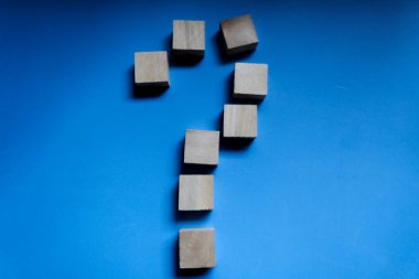 Ahşap blok mavi arkaplanda bir soru işareti oluşturuyor