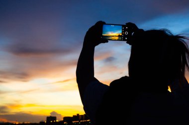 Plajda gün batımına cep telefonuyla bakan bir kadın. Tack fotoğraf silueti rahatlatıcı