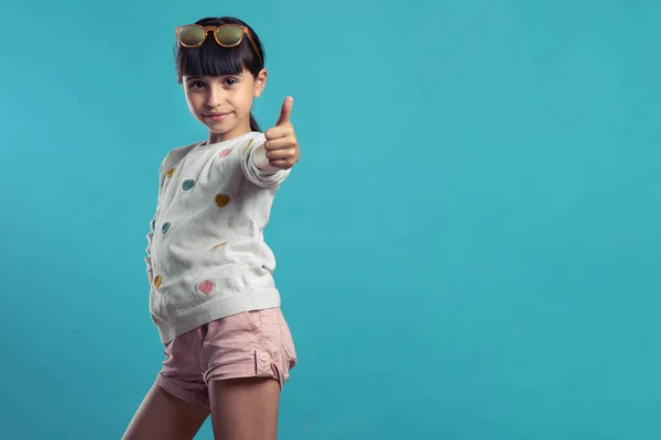 Kız, mavi arka planda başparmağıyla süper bir şey yapıyor.