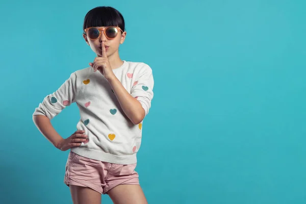 Şirin bir kız mavi arka planda susuyor.