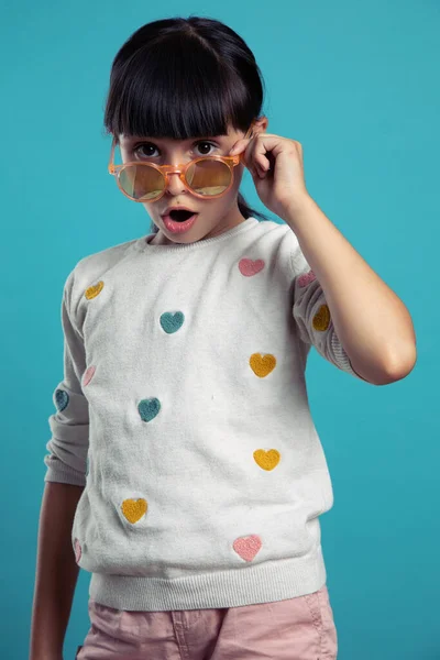 Mavi arka planda güneş gözlüğü takan hoş, şaşkın bir kızın portresi.