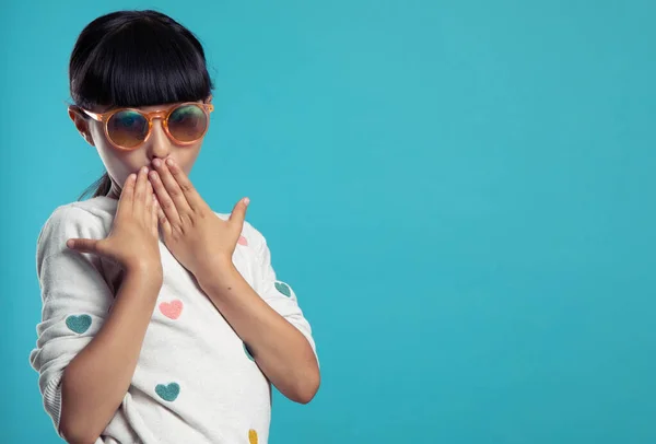 Mavi arka planda güneş gözlüğü takan hoş, şaşkın bir kızın portresi.