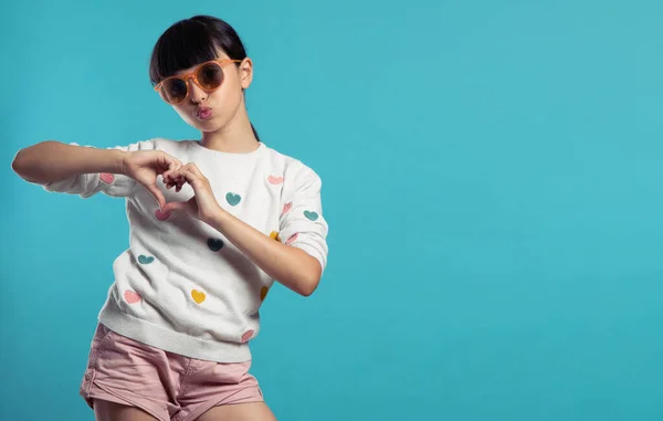 Güzel kız, elleri mavi arka planda kalp yapıyor.