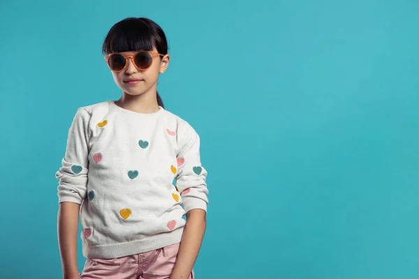 Mavi arka planda güneş gözlüğü takan sevimli bir kızın portresi.