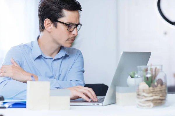 Gözlüklü bir adam ofisinde bilgisayarla ciddi şekilde çalışıyor.