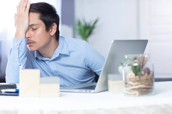 Yorgun adam elini alnına koyup ofiste çalışıyor.