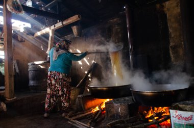 Kadınlar büyük kazanlarda pekmez pişiriyor, karanlık oda duman içinde.