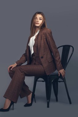 Gri arka planda esmer kadın modelin modadan minimalist portresi. İskoç renginde şık kıyafetler, kadın aksanlı beyaz ipek gömlek.