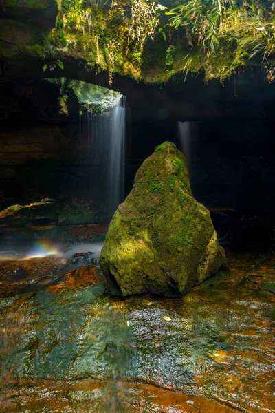 mossy stone with cave in the background with waterfall