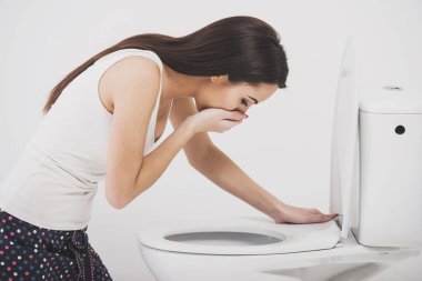 Young woman vomiting into toilet bowl clipart