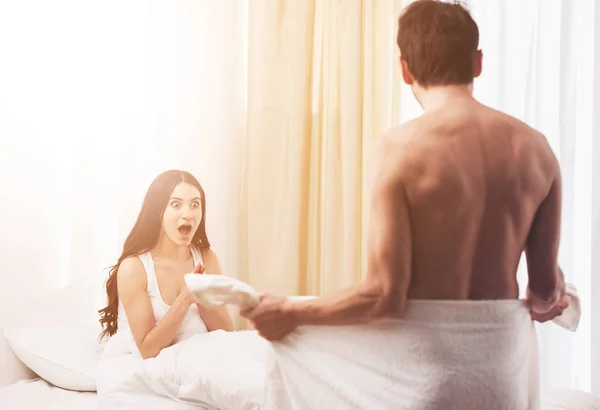 Menina chocada na cama olha para o homem — Fotografia de Stock