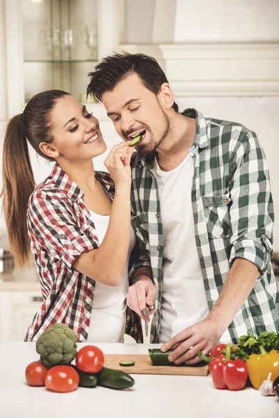 Vrouw feeds haar man met komkommer in comfortabele keuken. — Stockfoto