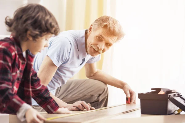 Abuelo y nieto miden mesa con cinta métrica . — Foto de Stock