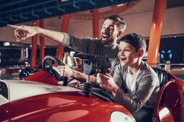 Smiling father and son sitting on toy car. Spending holiday together with family. Entertainment center, mall, amusement park. Family rest, leisure concept. clipart