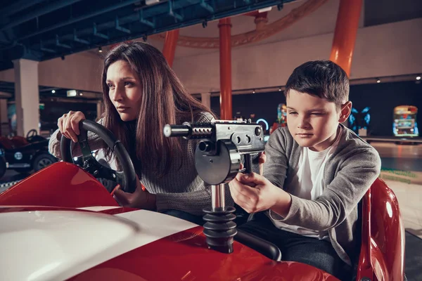 Concentrated mother and son driving toy car. Spending holiday together with family. Entertainment center, mall, amusement park. Family rest, leisure concept.