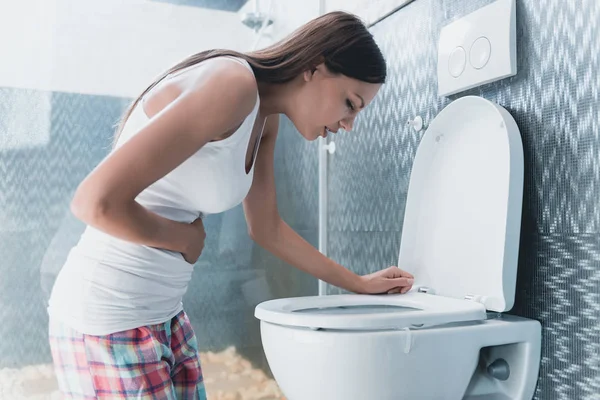 Joven chica doblado abajo cerca de inodoro en cuarto de baño . —  Fotos de Stock