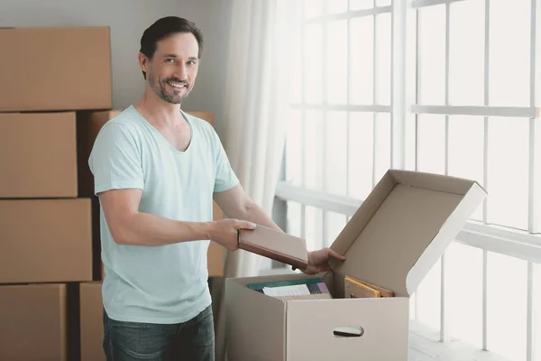 Happy Young Guy desempaca la caja de cartón en la habitación . — Foto de Stock