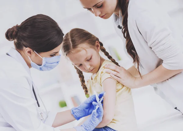 Junge Ärztin in Maske impft kleines Mädchen. — Stockfoto