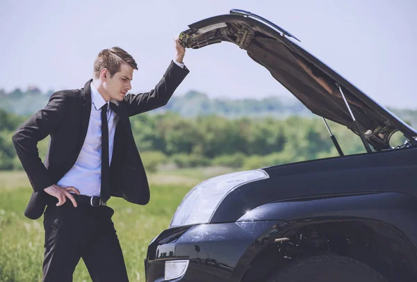 Беспокойный молодой бизнесмен, осматривающий сломанный автомобиль . — стоковое фото