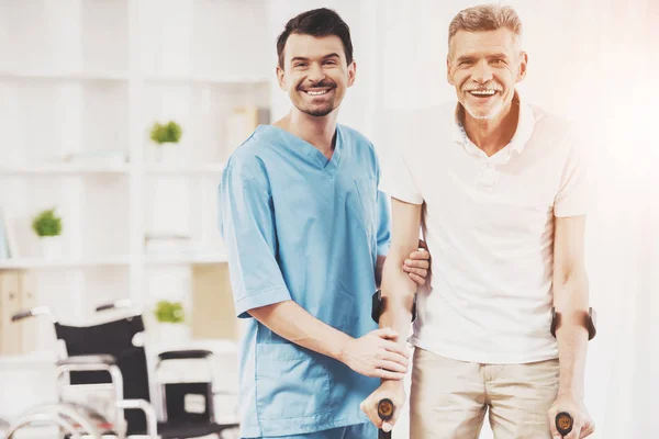 Sorridente medico aiuta vecchio paziente con stampelle — Foto Stock