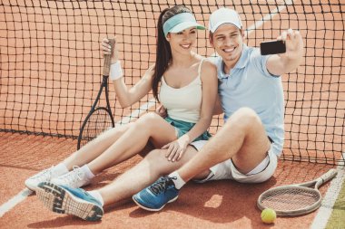 Raketleri ile tenis kortunda oturan oyuncular.