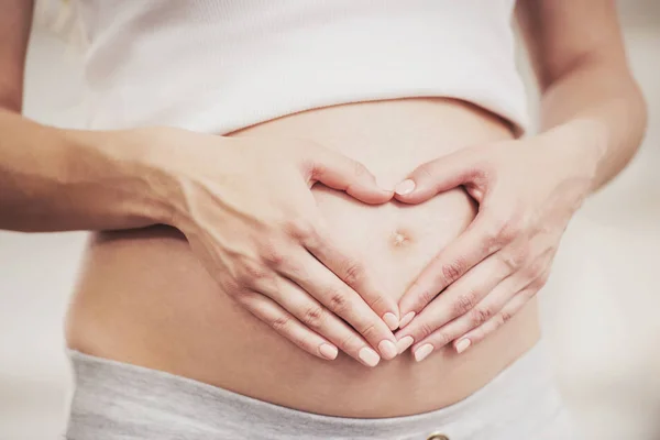 De cerca. Embarazada chica muestra corazón con sus manos — Foto de Stock