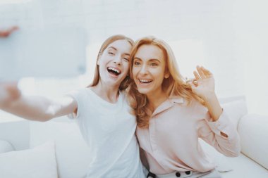 Anne ve genç kızı kanepeye Selfie alarak. Kız ile Smartphone. Anne-baba ve çocuk arasındaki iletişim. Mutlu anne ve kızı. Beyaz koltuk üzerinde gülümseyen kadın. Dijital Gadget'ı kullanma.