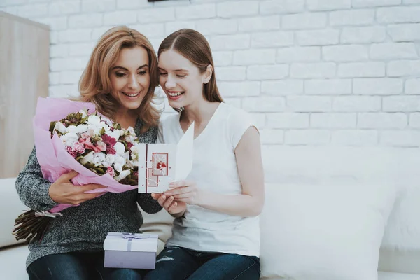 Smiling Daughter Gives Mother Flowers and Gift. Relationship in Family. Holiday at Home. Happy Mother. Friendly Relations. Celebrating Together. Happiness in Family Concept. Presenting Gift.