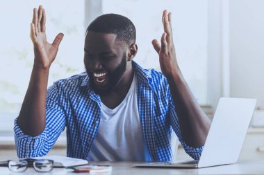 Masada oturan gülen genç Afro-Amerikan adam.