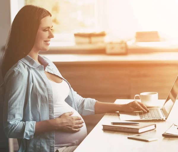 Jeune femme enceinte souriante utilisant un ordinateur portable à la maison . — Photo