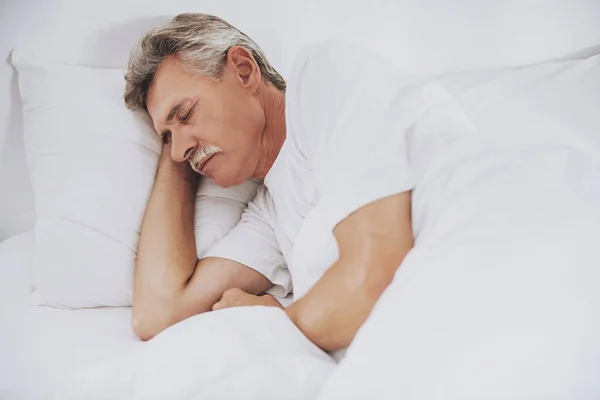 Παλιά ο άνθρωπος στον ύπνο στο άνετο κρεβάτι στο σπίτι με το λευκό. — Φωτογραφία Αρχείου