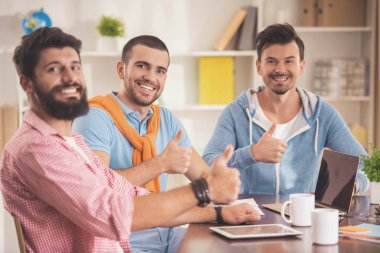 Dizüstü bilgisayar ile odada üç genç gülümseyen adam .