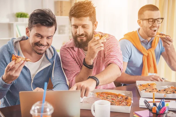 Les jeunes hommes regardant dans un ordinateur portable et mangeant de la pizza . — Photo