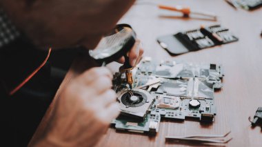 Yakın çekim. Tamiri anakart Pc. tamircisi ihtiyar. Araçları ile çalışan. Bilgisayar donanım. Büyüteç Camı. Havya. Dijital aygıt. Laptop üstünde okul sırası. Elektronik cihazlar kavramı.