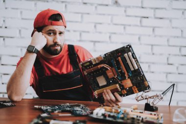 Atölye kırık anakartlar genç adam kırmızı şapkalı. Modern atölye kavramı. Üretim aracı. Modern araçları kavramı. Elektronik cihazlar kavramı. Mobil aygıt donanım. Ahşap Resepsiyon.