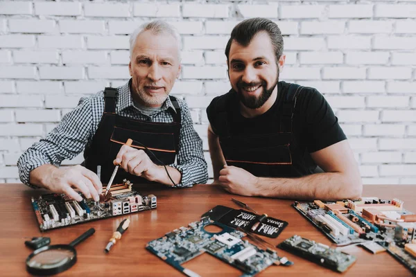 Two Men Repairing Hardware Equipment from PC. Repair Shop. Worker with Tools. Computer Hardware. Young and Old Workers. Soldering Iron. Digital Device. Laptop on Desk. Electronic Devices Concept.