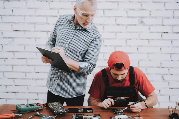 Old Manager Checking Motherboard near Worker. Worker with Tools. Computer Hardware. Young and Old Workers. Modern Devices. Digital Device. Wooden Table. Electronic Devices Concept.