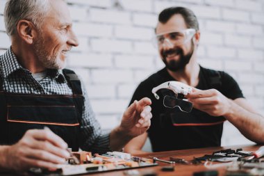 Donanım ekipmanları atölyesinde tamir iki adam. Dükkanı onarın. Araçları ile çalışan. Bilgisayar donanım. Genç ve yaşlı işçi. Modern cihazlar. Dijital aygıt. Laptop üstünde okul sırası. Elektronik cihazlar kavramı.