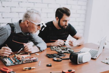 İki adam Pc. onarım donanım ekipmanları tamir dükkanı. Araçları ile çalışan. Bilgisayar donanım. Genç ve yaşlı işçi. Modern cihazlar. Dijital aygıt. Laptop üstünde okul sırası. Elektronik cihazlar kavramı.