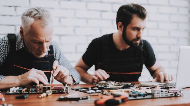 İki adam Pc. onarım donanım ekipmanları tamir dükkanı. Araçları ile çalışan. Bilgisayar donanım. Genç ve yaşlı işçi. Modern cihazlar. Dijital aygıt. Laptop üstünde okul sırası. Elektronik cihazlar kavramı.