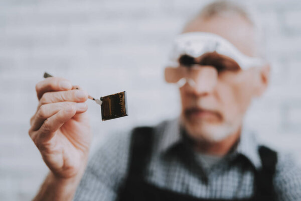 Elderly Man with Special Glasses in Repair Shop. Worker with Tools. Magnifying Glass. Worker in Glasses. Worker in Black Uniform. Man with Gray Hair. Modern Workshop Concept. Engineer in Uniform.